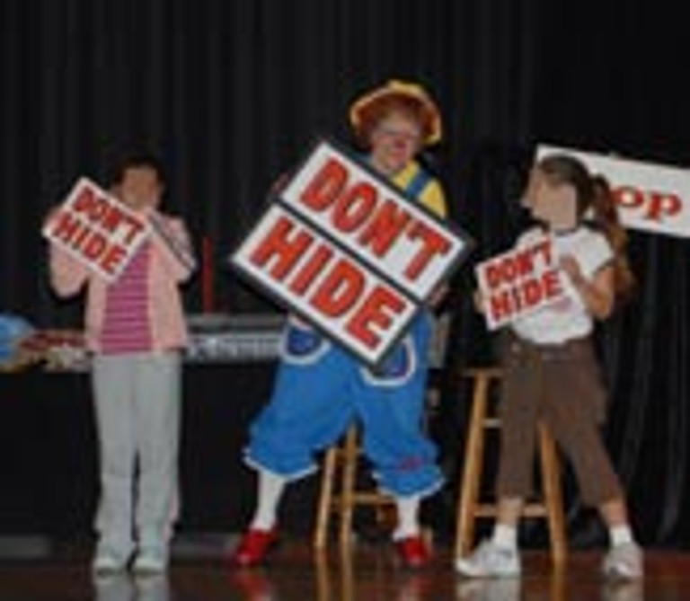 Rainbow and two children hold signs that say "Don't Hide"